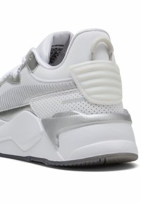 Vit sneaker med en texturerad silveröverdragning, en vadderad hälflik och perforerade detaljer. Har gummisula och snörningssystem.