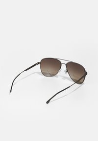 Occhiali da sole aviator con montatura in metallo. Lenti sfumate marroni. Lungo bracci neri che si assottigliano verso le punte. Naselli regolabili.