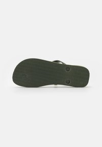 Temnozeleni podplat sandal z teksturno površino, ki vključuje dva krožna utora za boljši oprijem, zasnovan za udobje in stabilnost.
