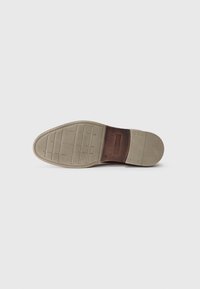 Semelle de chaussure en cuir marron avec une semelle extérieure en caoutchouc beige texturé. Présente un accent en cuir lisse et des motifs de semelle pour l'adhérence.
