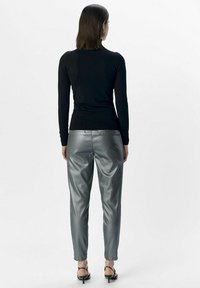 Zwarte aansluitende coltrui gecombineerd met metallic zilveren broeken, met een soepele textuur en een taps toelopend ontwerp, aangevuld met zwarte hoge hakken sandalen.