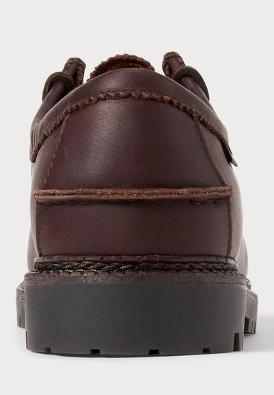 Zapato de cuero marrón con un talón redondeado, costuras contrastantes y una suela robusta de goma negra. Cuenta con un asa para facilitar su uso.
