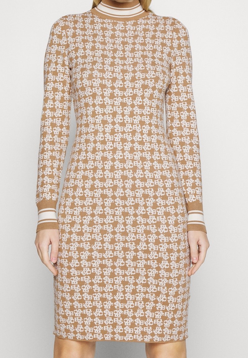 Robe marron en tricot avec motif géométrique blanc, manches longues, col montant et accents rayés aux poignets et au col. Coupe ajustée.