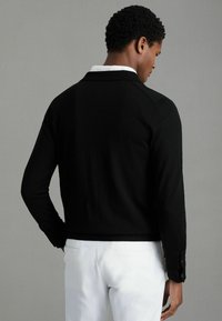 Cardigan negru tricotat, cu o croială ajustată, având mâneci lungi și un guler structurat. Asortarea cu pantaloni albi adaugă un contrast.