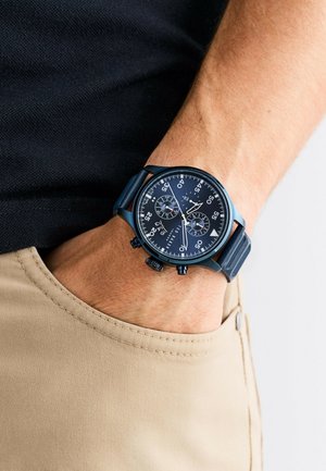 Chronografur med en mørkeblå urskive, sølvmarkører og gummirem. Har tre undertavler og en tekstureret kassefinish.
