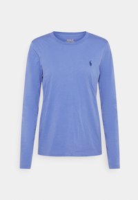 T-shirt à manches longues en coton bleu clair avec un col rond et un petit logo bleu foncé sur la poitrine gauche. Texture lisse.