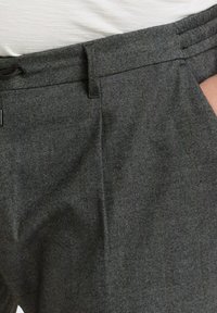 Close-up of dark gray pinstriped trousers with belt loops and a hand partially inside the pocket, against a white shirt background.