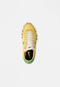Yellow sneaker with green accents, white laces, and textured black rubber sole. Features a logo on the heel and a padded tongue.
