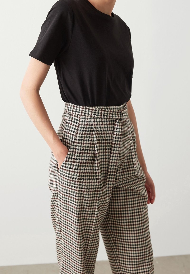 Černé tričko s krátkým rukávem v kombinaci s vysokými kostkovanými kalhotami v béžové, hnědé a černé barvě, které mají kapsy a volný střih.