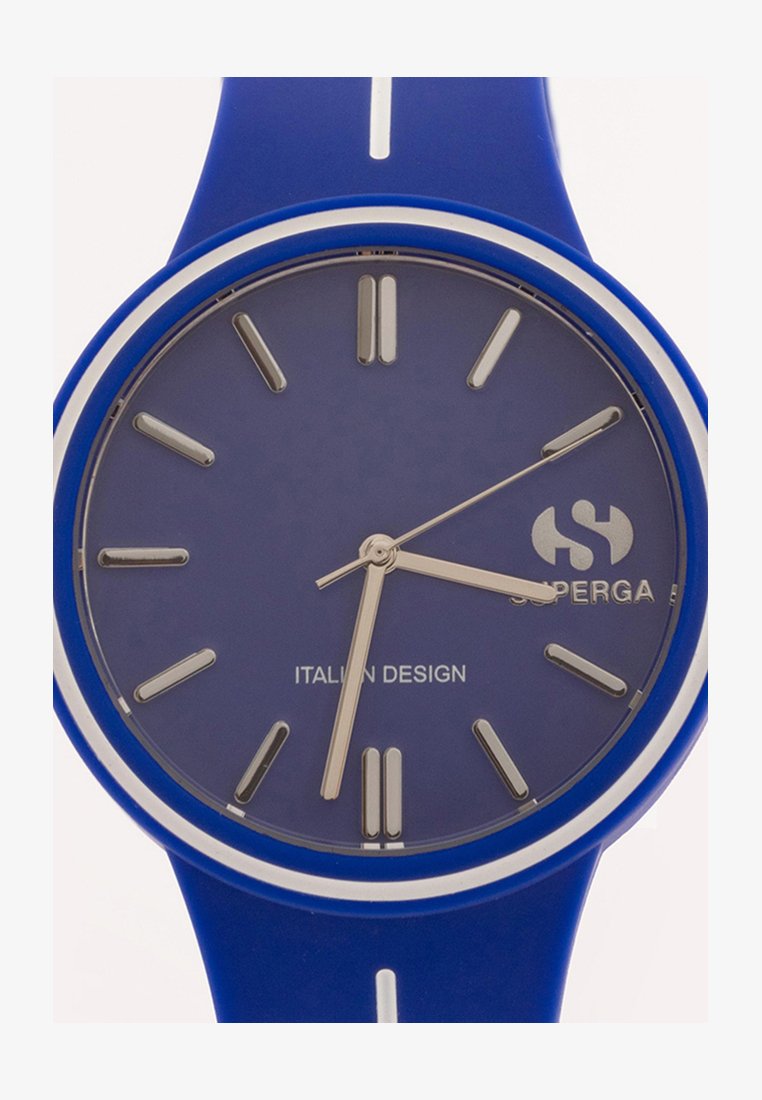 Sinine silikoonkell ümmarguse näoga, hõbedased numbrid ja tekst "ITAALIA DISAIN". Kellal on hõbedane ring kordinäidiku ümber.