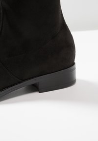 Czarne zamszowe botki za kostkę z masywnym obcasem i gładką fakturą. Projekt zawiera subtelne akcenty w postaci przeszyć oraz zaokrąglony nosek.