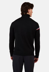 Schwarzer Rollkragenpullover mit geripptem Saum und Bündchen. Mit farblich kontrastierenden Streifen in Rot, Weiß und Blau an der Schulter. Strukturiertes Strickgewebe.