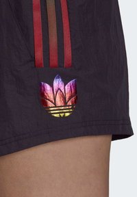 Černé šortky s třemi červenými vertikálními pruhy a vícebarevným reflexním logem Adidas s květinovým motivem. Texturovaná tkanina.