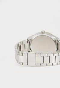 Reloj de acero inoxidable con un diseño de pulsera enlazada, que presenta una parte posterior de caja lisa y una corona en la parte superior para ajustar la hora.