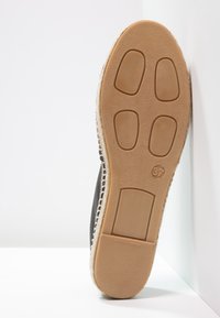 Suela de zapato tipo alpargata, goma beige con agarre texturizado, parte superior de tela negra con borde de yute, talla 37, inclinada para mostrar los detalles de la suela.