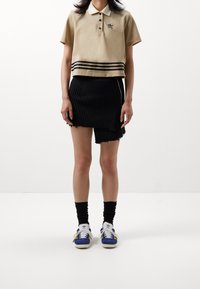 Beige polo triko s černými pruhy, černá žebrovaná minisukně s třepeným lemem a modré tenisky s bílými tkaničkami na jednobarevném pozadí.