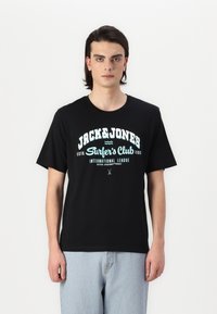 Juoda medvilninė marškinėliai trumpomis rankovėmis ir apvalia iškirpte. Priekyje yra balta ir turkio spalvos tekstas: „JACK&JONES Surfer's Club“ su grafikų akcentais.