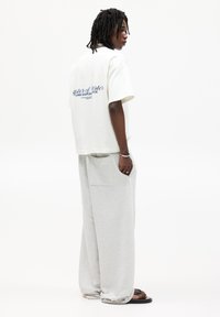 White cotton t-shirt with blue text on the back, paired with light grey wide-leg sweatpants featuring side pockets and a relaxed fit.