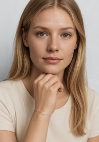 Bracciale d'argento con design a stella, caratterizzato da anelli e piccoli ornamenti. Il modello indossa una camicia beige chiaro, con la mano poggiata sul mento.