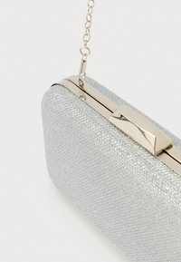 Carteira de mão prateada com superfície texturizada, alça de corrente fina e fecho metálico. Apresenta um padrão de diamante em todo o corpo.