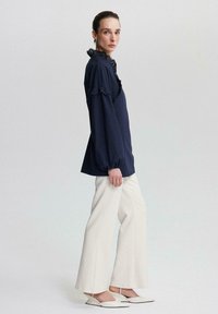 Tumed blouse rüüfitud krae, pikad varrukad ja pitsaktsendid, koos valgete laia säärega pükstega ning terava ninaga slingback kingadega.