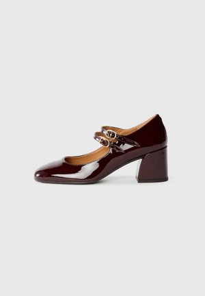 Zapatos de charol burdeos estilo Mary Jane con dos correas ajustables y hebillas en tono dorado, que cuentan con un tacón bloco y un diseño de punta afilada.
