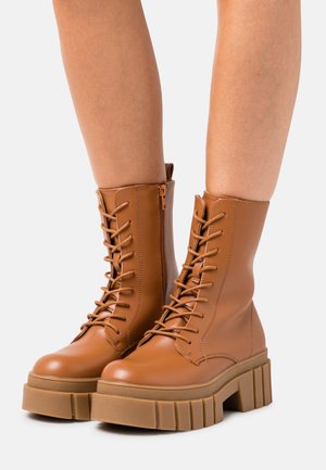 Botas de couro castanho com atacadores, apresentando uma sola plataforma robusta e fecho lateral com zíper, com detalhes cosidos e uma textura suave.