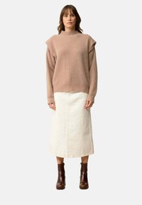 Roze gebreide trui met hoge kraag en geribbeld textuur, gecombineerd met een crèmekleurige midi-skirt en bruine enkellaarzen.