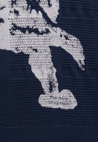 Primer plano de tela de punto azul marino con una figura abstracta blanca y texto impreso pequeño parcialmente visible en la parte inferior.