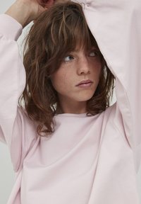 Felpa oversize rosa chiaro con scollatura tonda e maniche ampie. Texture liscia con dettagli di cucitura visibili.