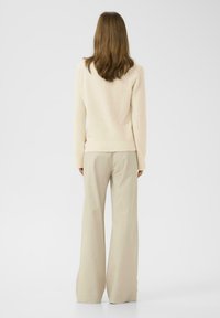 Pull en beige à manches longues et taille ajustée, associé à un pantalon ample en crème clair, créant une tenue douce et neutre.