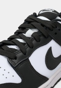 Gros plan sur une chaussure Nike en noir et blanc montrant des lacets noirs, des détails de couture et le logo Nike swoosh sur un matériau en cuir.