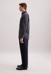 Camicia a maniche lunghe di colore blu scuro con un motivo floreale dettagliato, abbinata a pantaloni scuri su misura e scarpe stringate nere.