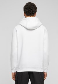 Hvid hættejakke med en stor, justerbar hætte. Lavet af blødt stof, med lange ærmer og lige nederkant, minimalistisk design.