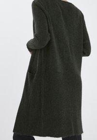 Mörkgrön kofta gjord av mjukt, strukturerat tyg, med en ribbad nederdel och sidofickor, designad med långa ärmar.