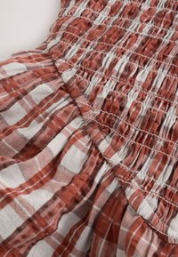 Tissu à carreaux rouille et blanc avec des détails de couture froncée et élastiquée créant une texture froncée sur un matériau doux.