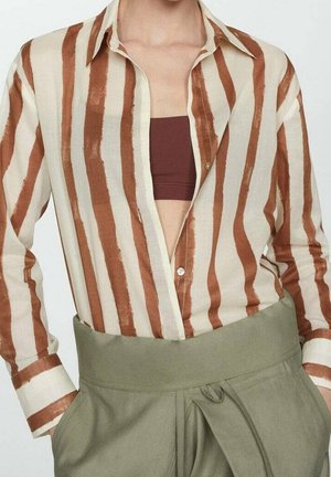 Person iført en beige og brun lodret stribet skjorte over en bordeaux crop top kombineret med højtaljede olivengrønne bukser med et stofbælte.