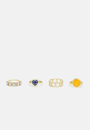 Conjunto de quatro anéis de ouro: um com pedras claras, um coração azul com um sorriso, um design entrelaçado e um sol amarelo com um sorriso.
