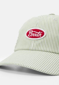 Ribaga roheline müts punase ja valge broderi "Brixton" logoga. Omab pehmet kangast, kumerat visiiri ja reguleeritavat tagaosa rihma.