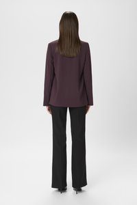 Blazer viola scuro con una texture liscia, abbinato a pantaloni neri a gamba larga; entrambi i capi presentano linee pulite e un minimalismo nei dettagli.