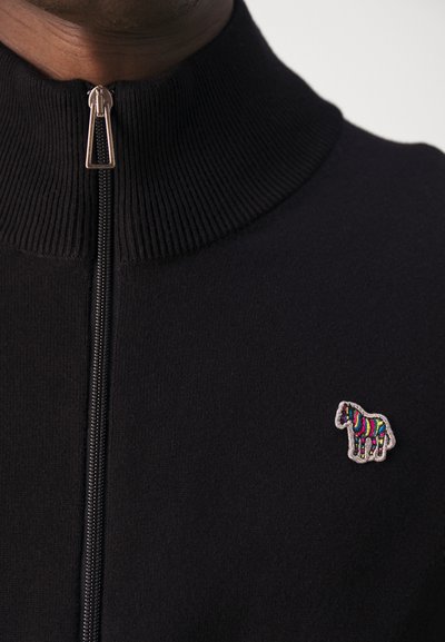 Black zip-up sweater with a ribbed collar and a colorful embroidered zebra logo on the left side. Soft knit texture visible.