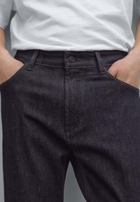 Mörk denimjeans med slim fit, med knappstängning, framfickor och subtila sömdetaljer. Materialet har en jämn textur.