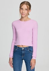 Jasnoróżowy, krótki, prążkowany sweter z długimi rękawami, okrągłym dekoltem i teksturowanym wykończeniem, zestawiony z ciemnoniebieskimi dżinsami.