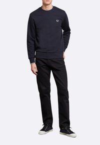Felpa della marina con colletto a costine, logo ricamato sul petto, abbinata a pantaloni neri e sneakers nere con suole bianche.