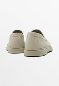 Une paire de chaussures slip-on en cuir texturé beige avec des semelles plates, vue de dos sur un fond blanc.