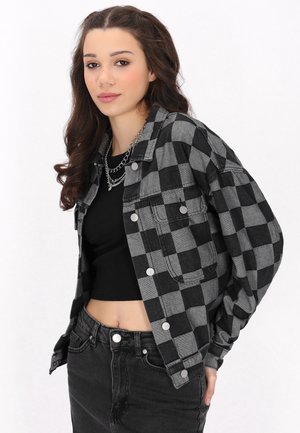 Zwart en grijs geruite flanellen jas met drukknoopjes en borstzakken, gedragen over een zwarte crop top en zwarte hoog-was jeans.