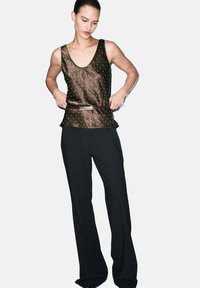 Pantalones negros fluidos combinados con una parte superior sin mangas oscura y brillante que presenta un patrón texturizado y puntos adornados. Modelo llevando un cinturón.