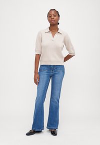 Lys beige kortermet collaret genser kombinert med lyseblå vide jeans og svarte spisse sko. Jevn tekstur, ingen mønstre.