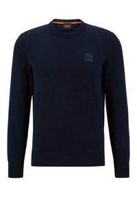 Donkerblauwe gebreide trui met een ronde halslijn, ribgebreide manchetten en onderrand. Bevat een gestructureerde logopatch op de borst en een oranje accent bij de kraag.