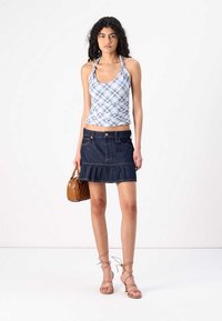Top sin mangas a rayas en azul y blanco, de diseño ajustado. Falda de mezclilla oscura con volantes, de longitud a medio muslo. Bolso de mano tejido en tono beige y sandalias nudistas.